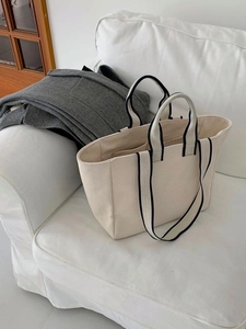 Detailed close-up of a beige canvas tote bag with contrast woven blue and white handles