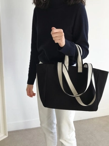 Detail shot of a black canvas tote bag with beige woven handles worn by a fashion model
