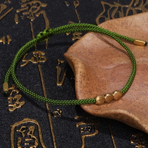 Detail of green hand-woven rope bracelet with three golden heart-shaped metal beads
