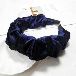 Detail of dark blue velvet pleated headband on a white decorative plate with paper
