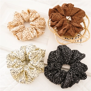 Detail of four fabric hair scrunchies with black polka dot patterns in neutral earthy tones