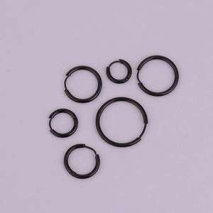 Set of six black stainless steel hoop earrings in various sizes on a purple background