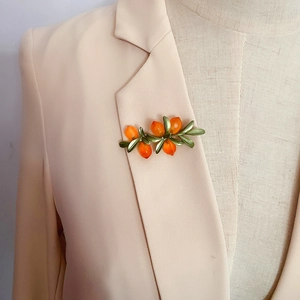 Close-up of orange glass berry brooch pinned on a beige blazer collar for styling