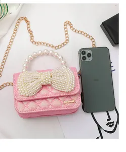Mini pink glitter crossbody bag with pearl bow detail shown next to a smartphone
