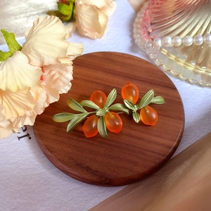 Detail view of orange glass berry brooch with green leaves on a rustic wooden coaster
