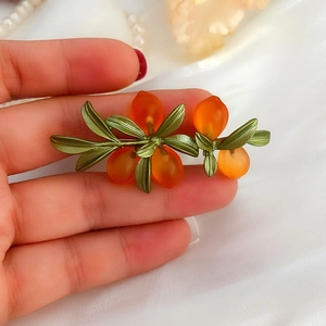Detailed view of handmade orange glass fruit brooch with green leaves on silk fabric