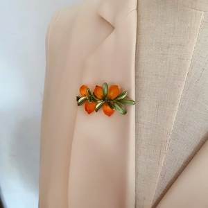 Detail of an orange flower brooch with green leaves pinned on a beige blazer lapel