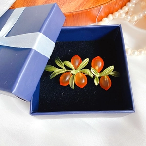 Detailed view of orange glass berry brooch with green leaves in a blue gift box
