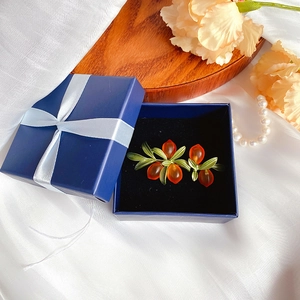Detailed view of olive branch leaf earrings with orange glass berries in a gift box