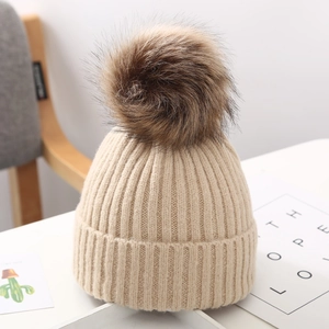 Primer plano del gorro de punto beige para bebé con pompón grande de piel sintética