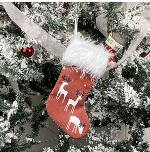 Close-up of burlap Christmas stocking with white deer print hanging on a snowy festive tree