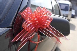 Macro detail of a large red organza ribbon bow tied to a car side mirror for wedding decor