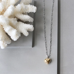 Gold heart pendant on silver paperclip chain necklace over minimalist stone display