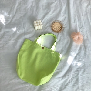 Close-up of light green corduroy tote bag with magnetic metal clasp on white linen