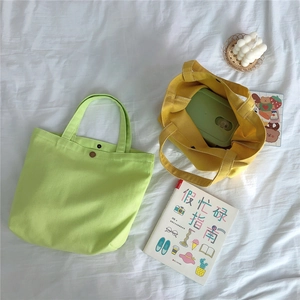 Top view of bright green and yellow canvas lunch bags with metal snap button on white fabric