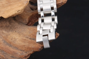 Macro detail of brushed stainless steel watch band buckle against a natural wood texture
