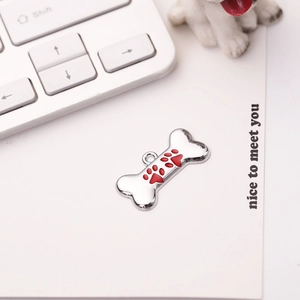 Close-up of bone-shaped silver dog tag with red enamel paw prints on a white background