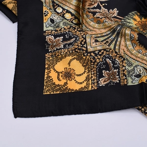 Detailed close-up of paisley print silk scarf with black, gold and beige patterns