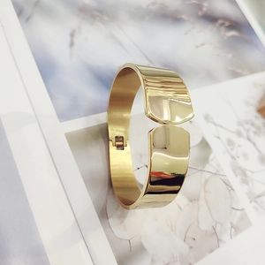 Close-up of a wide gold-plated stainless steel bangle with polished mirror finish
