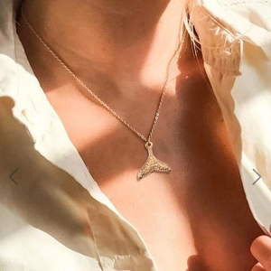 Elegant gold mermaid tail pendant necklace on model with textured fishtail charm