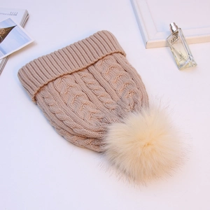 Close-up of cable knit beanie with faux fur pompom and ribbed cuff in beige