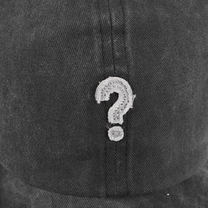 Dettaglio macro della toppa con punto interrogativo bianco su cappello denim grigio