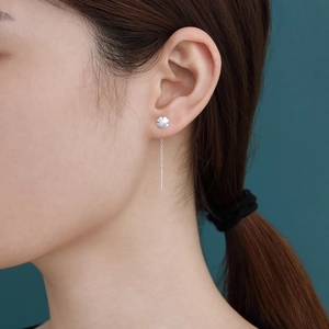 Model wearing elegant silver S925 four-leaf clover tassel earrings on a teal background