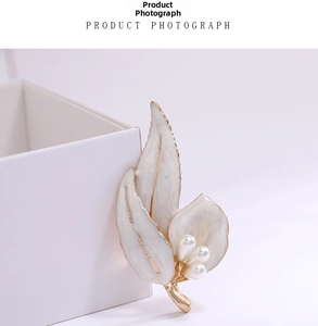 Detail of white enamel leaf brooch with golden edges and three pearls on jewelry box