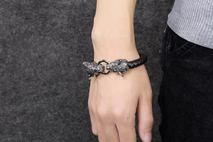 Détail d'un bracelet en cuir noir tressé avec double tête de loup en acier porté au poignet