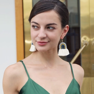 Détail de boucles d'oreilles bohèmes à franges crème avec motifs tissés bleu et jaune