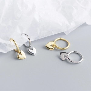 Close-up of heart charm earrings in gold and silver finish on a textured background