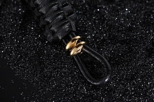 Close-up of black braided leather texture and polished gold metal anchor clasp