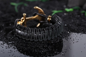 Macro shot of black woven leather strap with a polished golden anchor-shaped metal clasp