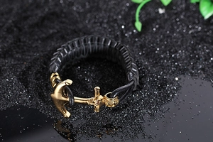 Close-up of black braided leather bracelet with golden anchor clasp on dark sand