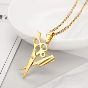 Detail shot of golden scissor and comb pendant necklace with rhinestone on ceramic tray