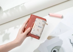 Detail of PU leather wallet with leaf print and gold Forever buckle on white desk