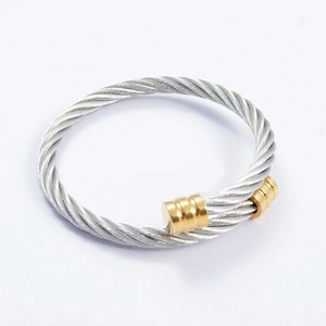 Détail de la texture du câble d'acier argenté torsadé et des embouts dorés sur le bracelet