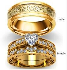 Close-up of gold couple ring set featuring dragon pattern male band and heart crystal female ring