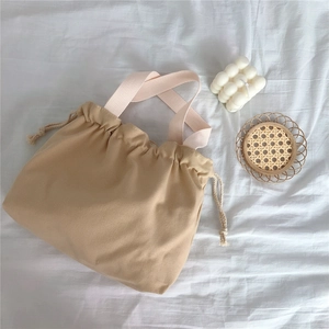 Detail of khaki canvas drawstring tote bag with cream ribbon handles on white cloth