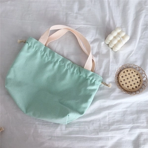 Detail of mint green canvas handbag featuring drawstring closure and cream-white handles