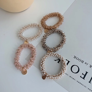 Detailed shot of five high-elastic beaded hair ties in neutral tones with metal charms