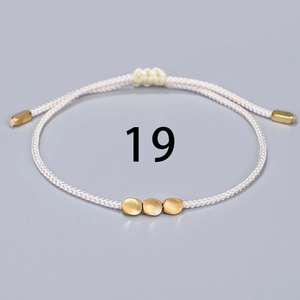 Close-up of cream woven bracelet with three golden beads and adjustable drawstring