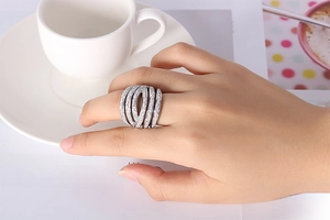 Detail of silver multi-layer crisscross ring with pavé diamonds on a hand holding a cup