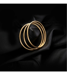 Three-piece set of minimalist gold polished stainless steel bangles on black leather background
