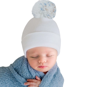 Close-up of soft knitted newborn hat with a fluffy pompom on a sleeping baby