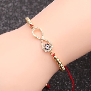 Infinity evil eye bracelet with gold beads and red cord on a dark shimmering background