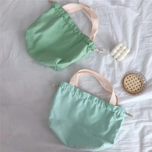 Detail of two canvas drawstring bags in vibrant green and mint shades on soft fabric