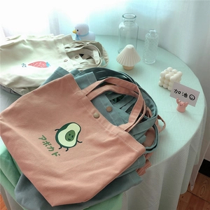 Stapel süßer Canvas-Taschen mit Avocado- und Erdbeerdruck auf einem Pastelltisch