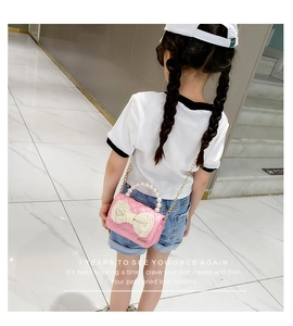 Rear view of pink quilted crossbody bag with pearl bow and gold chain on young model