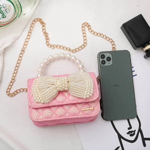 Pink glitter mini girls bag with large pearl bow and gold chain strap shown next to a phone